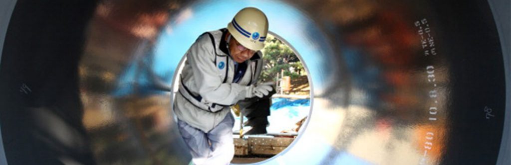 A worker inspects a steel pipe during pipe replacement in Japan