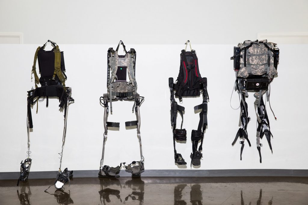 Four different types of exoskeletons for workers and military personnel hang on display.