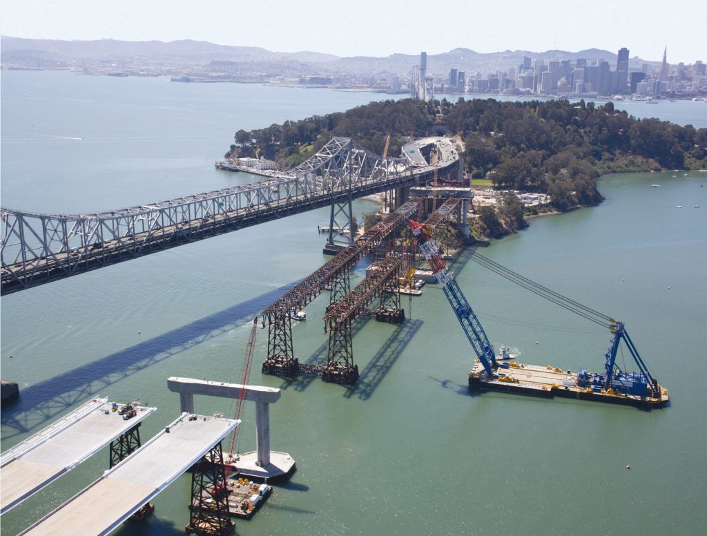A floating crane lifts prefabricated deck sections onto the San Francisco-Oakland Bay Bridge.