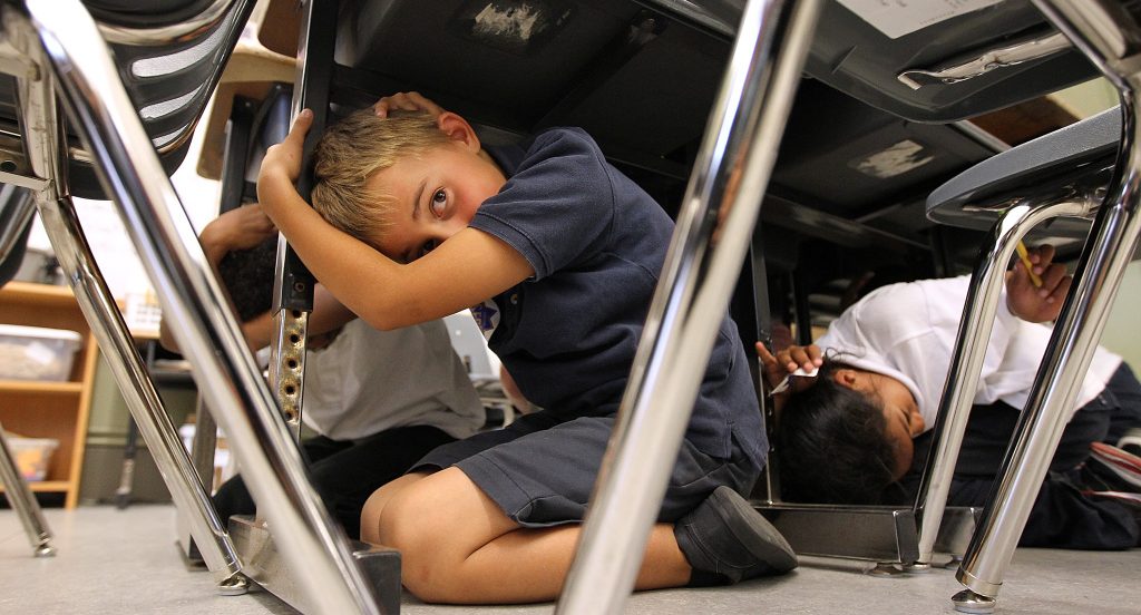 A young boy takes cover under his desk during an earthquake drill.