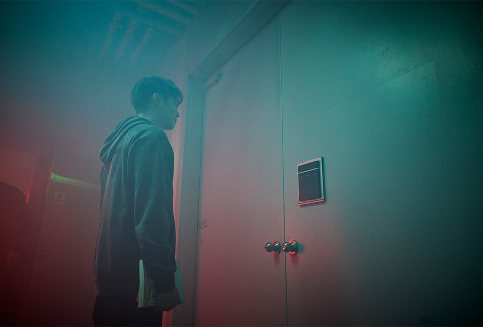 문앞에 서서 비밀번호를 입력하는 패드를 응시하고 있는 조윤우 배우의 모습