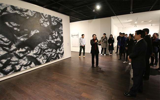  김윤희 큐레이터가 '제4회 신진작가 공모'展' 개막식 행사에 참석한 관람객들에게 심윤 작가 <박쥐떼, Oil on canvas, 259x450cm, 2017> 작품에 대해 설명하고 있다.