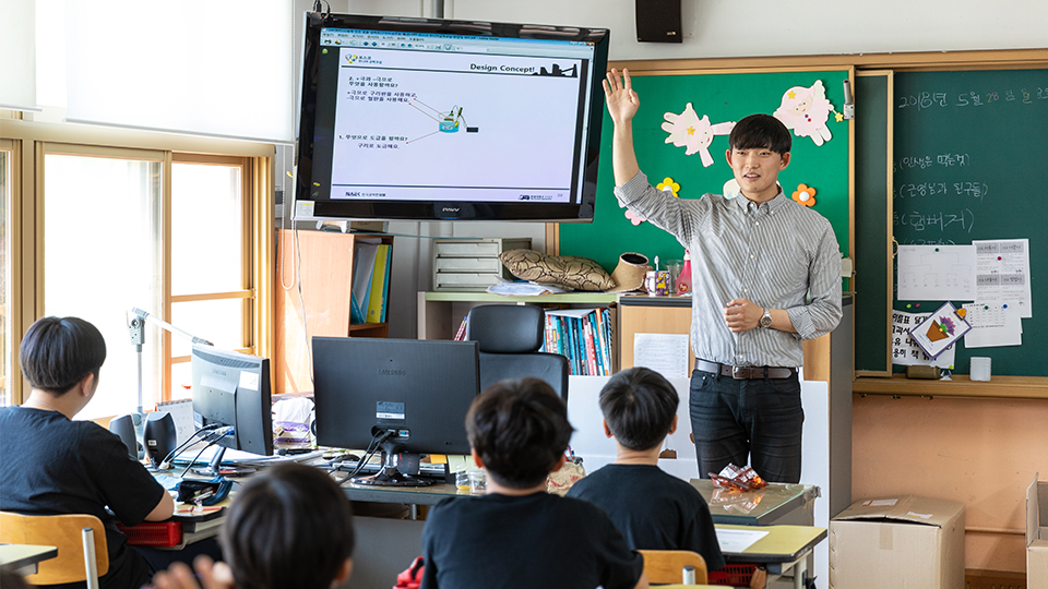 포스코 주니어공학교실에서 대학생 강사가 앞에 나와 손을 들고 있는 모습 