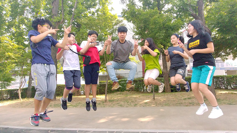 봉사단원과 아이들이 공원에서 높게 점프하는 순간을 찍은 사진
