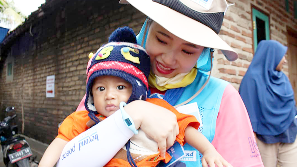 귀여운 모자를 쓴 현지 어린이를 봉사단원이 안고 있는 모습 