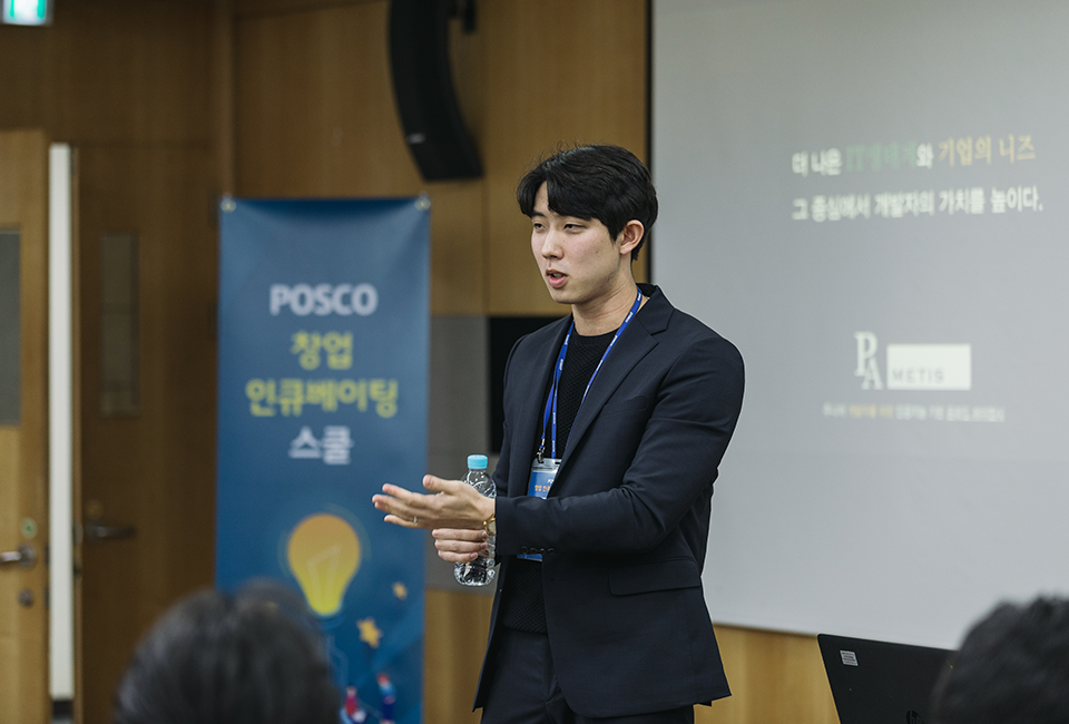 POSCO 창업 인큐베이팅 스쿨 교육생 한 명이 "더 나은 IT생태계와 기업의 니즈, 그 중심에서 개발자의 가치를 높이다"가 표출된 스크린 앞에서 발표하는 모습