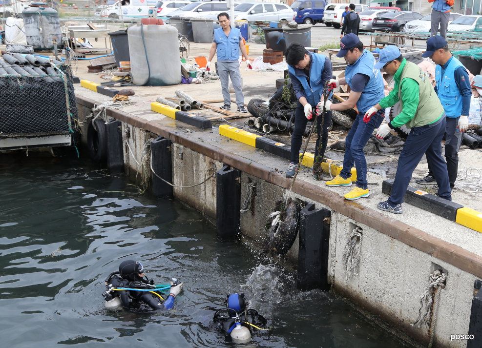 잠수복을 입은 두 사람이 바다에서 지상으로 봉사단에게 전달하는 모습. 항구에서 폐타이어를 수거해 지상 봉사자에게 전달하는 포스코 클린오션봉사단