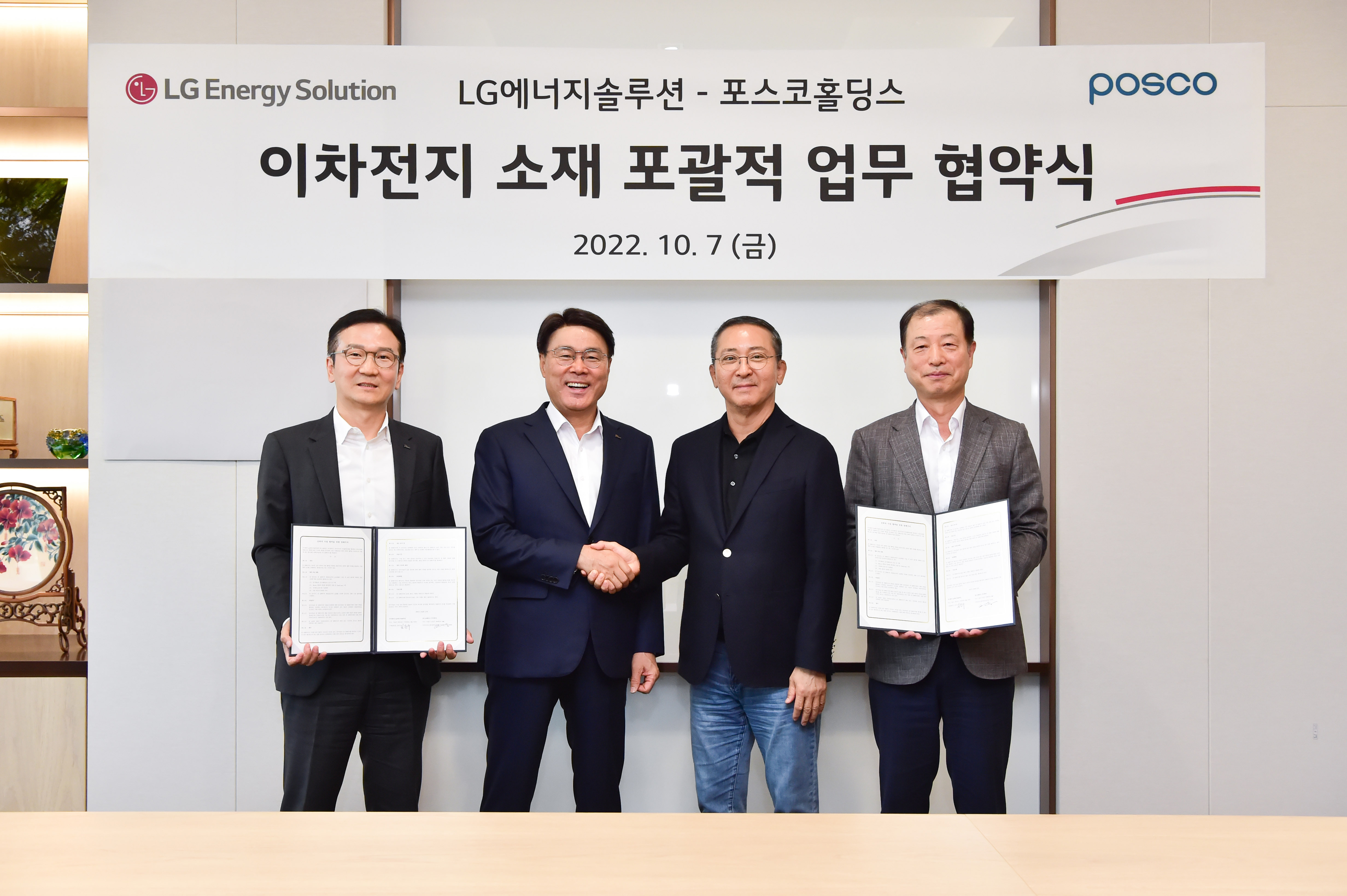 LG 에너지솔루션과 포스코홀딩스가 이차전지 소재 포괄적 업무 협약식에서 협약을 맺고 현수막 앞에서 협약서를 들고, 악수를 하며 찍은 사진이다. 네명의 남자가 서있고 양끝에는 협약서를 가운데는 악수를 하고 있다.