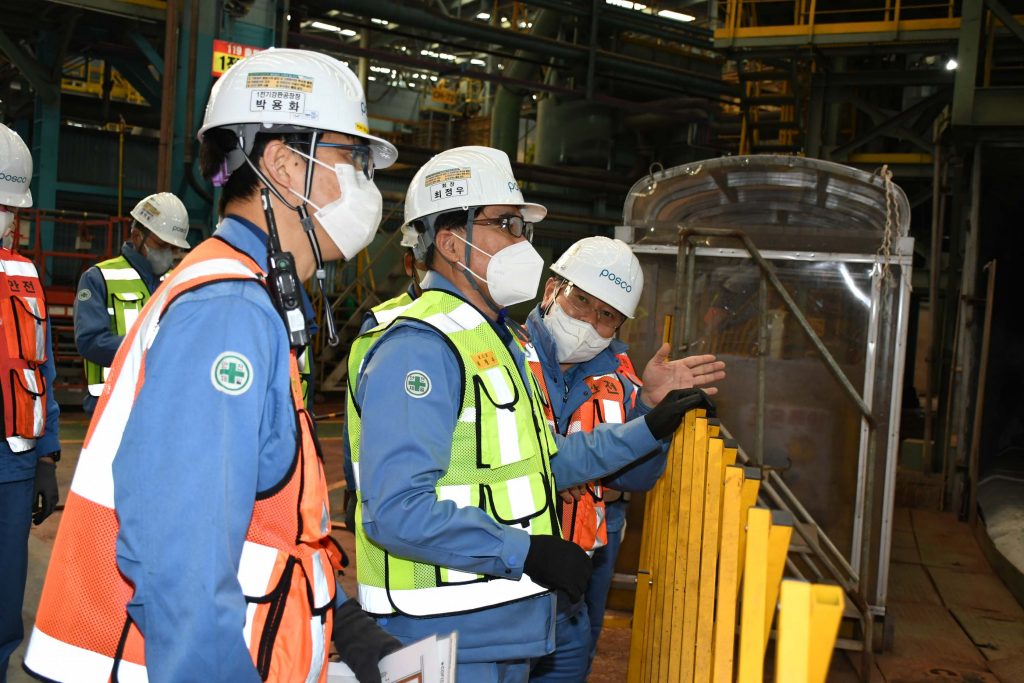 흰 작업모와 파란색 작업복, 안전조끼를 입은 남성 여러명이 공장 내부를 점검하고 있는 모습이다. 
