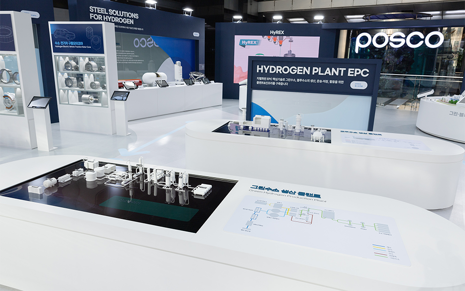 HYDROGEN PLANT EPC라고 쓰인 전시부스 안에 흰색의 공장 플랜트 미니 모형이 설치되어 있다. 