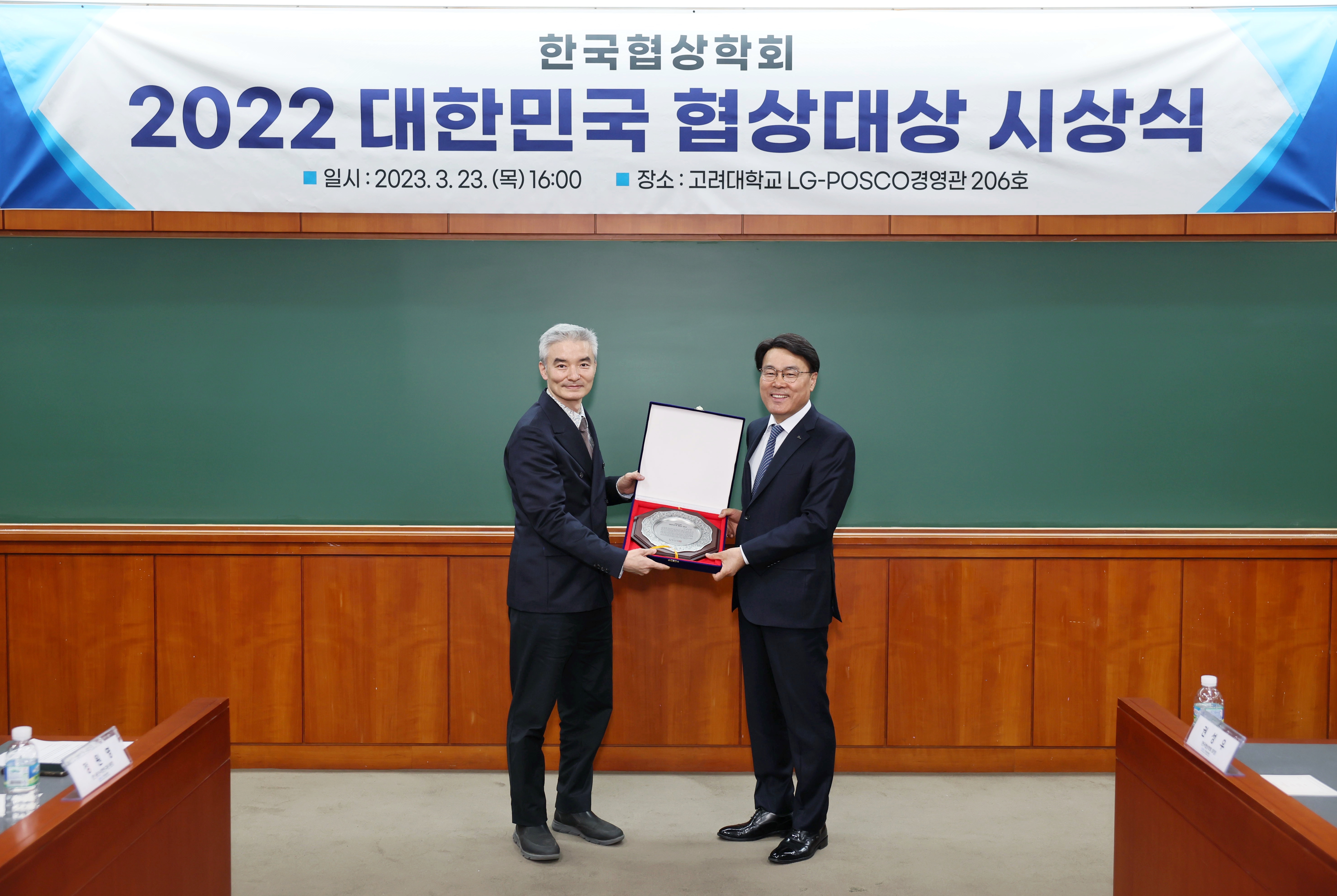 한국협상학회 2022 대한민국 협상대상 시상식 이라는 현수막 앞에서 정장 입은 두 남자가 함께 상패를 들고 기념촬영하고 있는 모습이다.