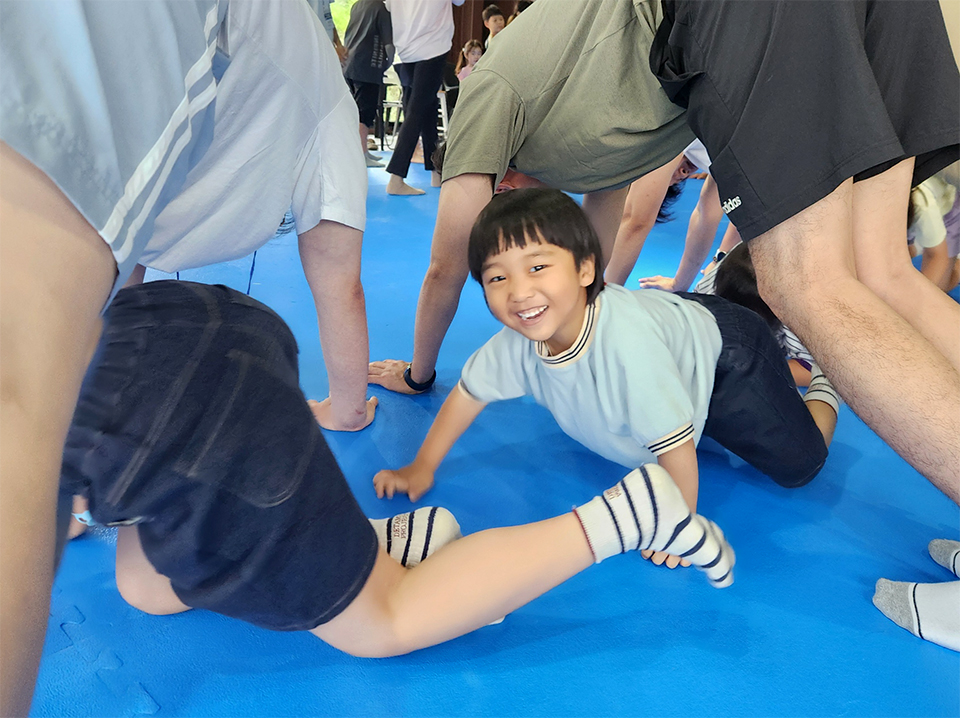 아빠 직원이 손으로 바닥을 짚고 터널을 만들자 그 밑으로 아이가 웃으며 지나가고 있다. 