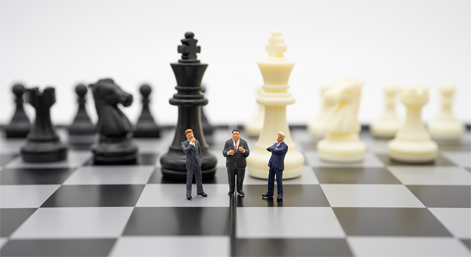 양복을 입은 남성 미니어처 인형 3명이 대형 흑백 체스판 위에서 토론을 하고 있다. 