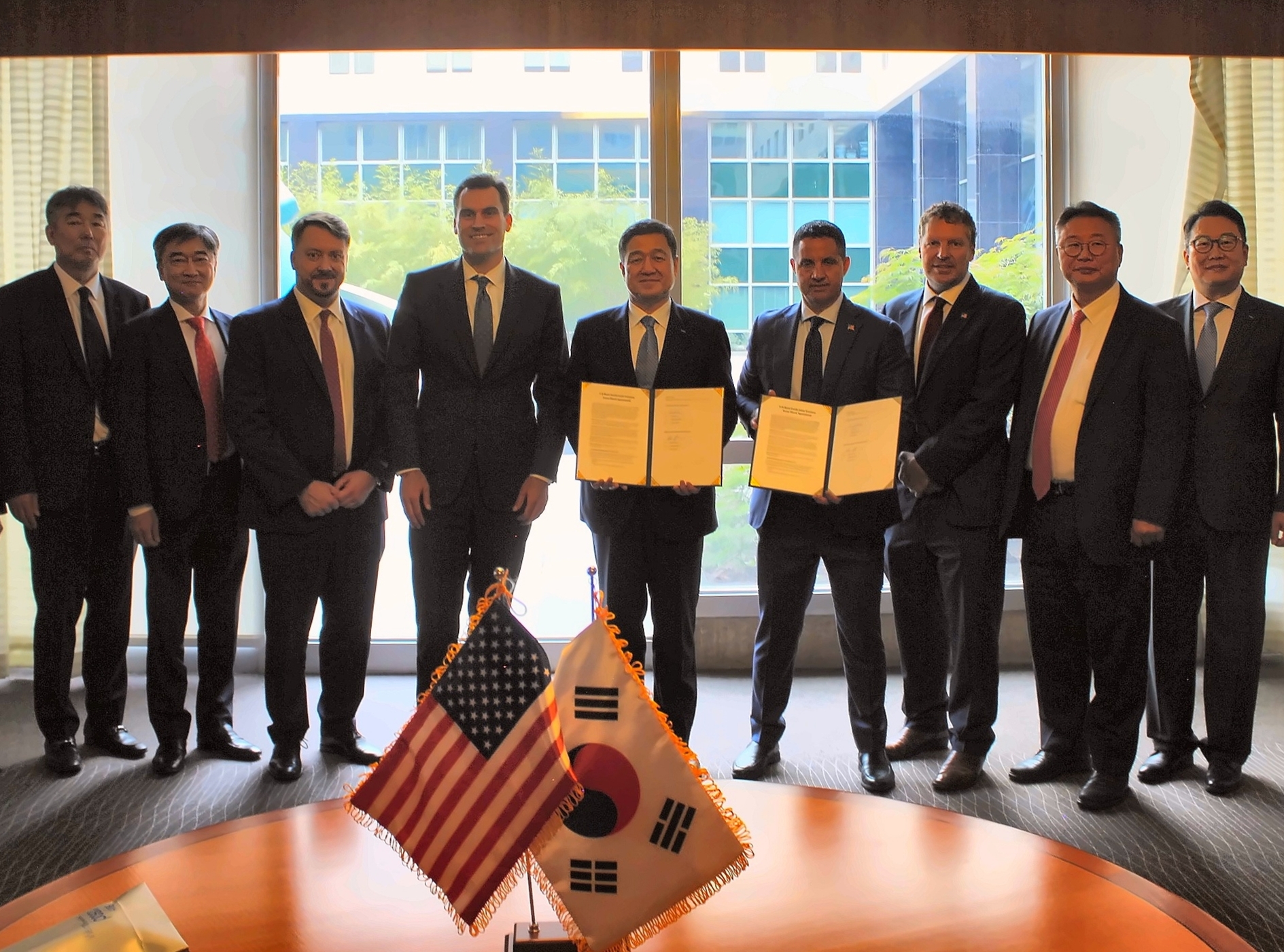 5월 21일(현지시간) 워싱턴 D.C.에서 美 리엘리먼트(ReElement Technologies Corporation)와 미국 희토류 분리정제 생산 합작법인 설립 추진을 위한 협약 체결식 모습이다. 9명의 관계자들이 증서를 들고 작은 미국,한국 국기 앞에서 기념촬영을 하고 있다. 