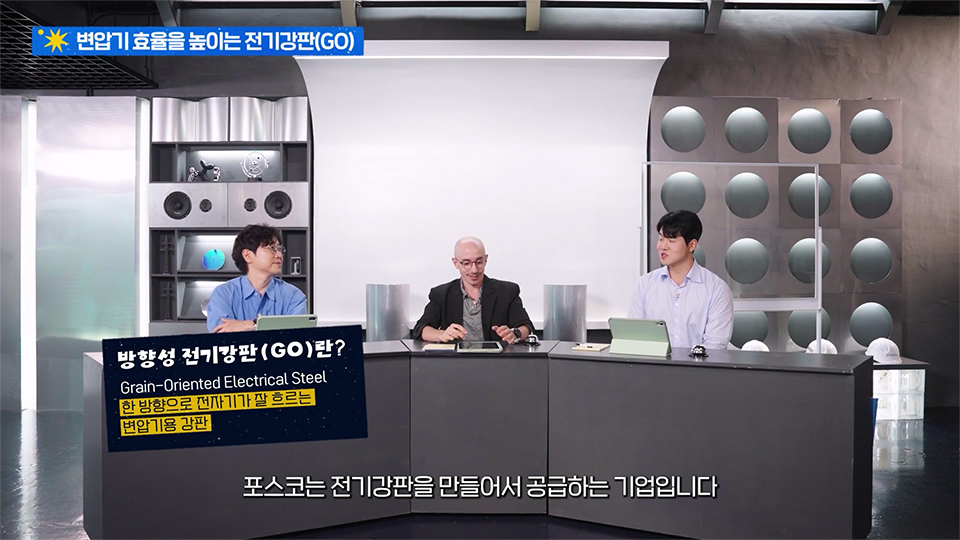 방향성 전기강판에 대한 대화를 나누는 세 사람 / 상단 제목 : 변압기 효율을 높이는 전기강판(GO) / 왼쪽 그래픽 설명 : 방향성 전기강판(GO)란? Grain-Oriented Electrical Steel - 한 방향으로 전자기가 잘 흐르는 변압기용 강판 / 하단 자막 : 포스코는 전기강판을 만들어서 공급하는 기업입니다.